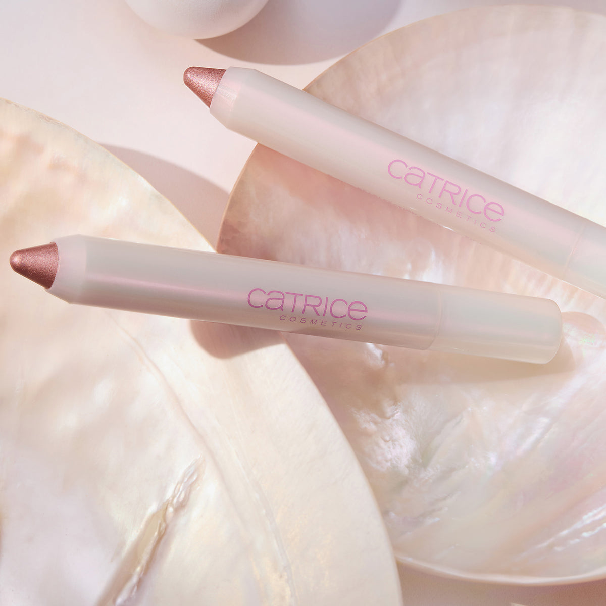 Zwei PEARLFECTION Eyeshadow Sticks von Catrice Cosmetics auf perlmuttartigen Muscheloberflächen.