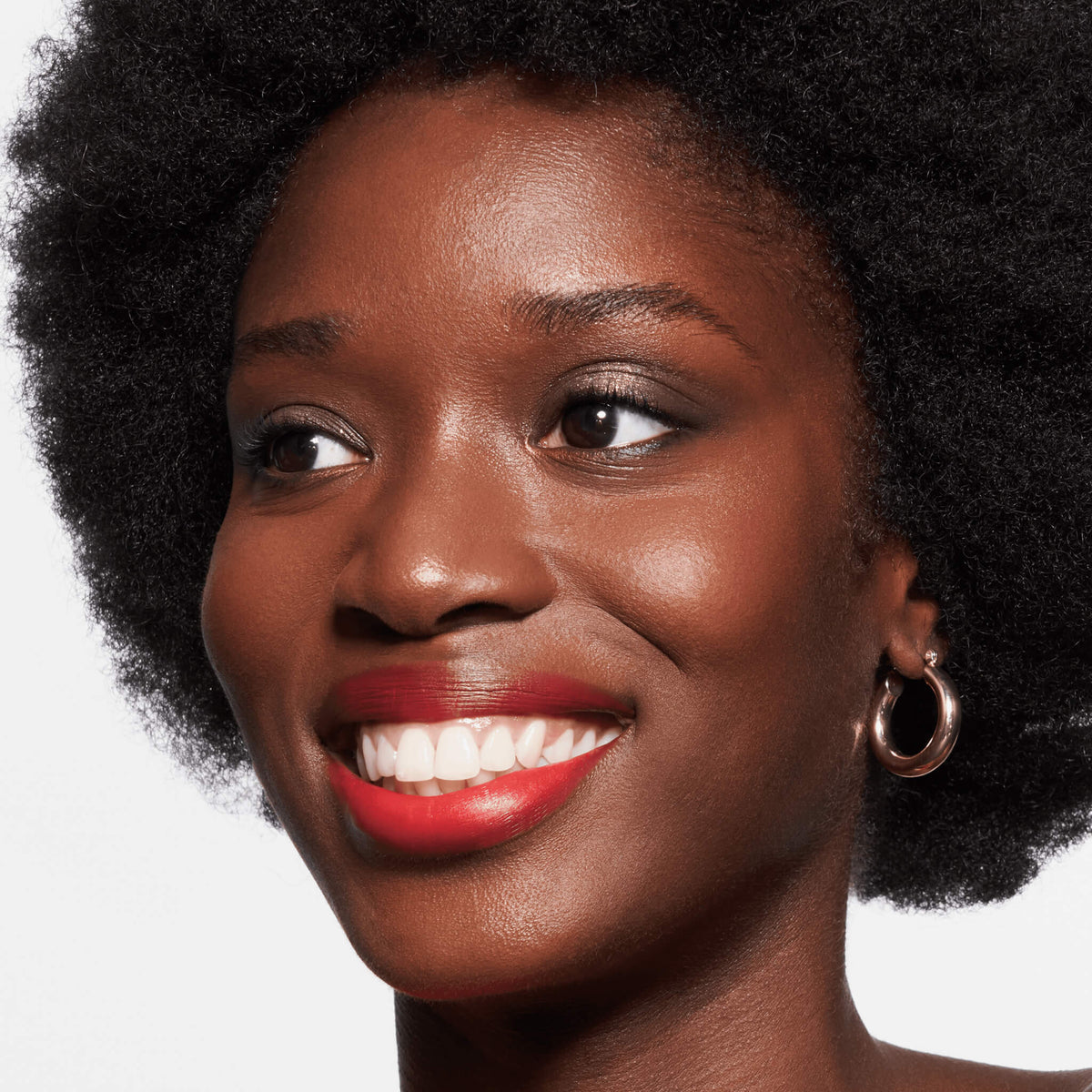 Eine lächelnde Frau mit Afro Creolen und rotem Lippenstift präsentiert den Slim'Matic Ultra Precise Brow Pencil Waterproof.