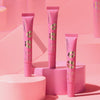 Drei KISS & GLOW Peptide Lip Tint C01-Tuben auf rosa geometrischen Plattformen vor einem rosa Hintergrund.