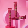 Drei Tuben KISS & GLOW Peptide Lip Tint C03 geometrischen Plattformen vor rosa Hintergrund.