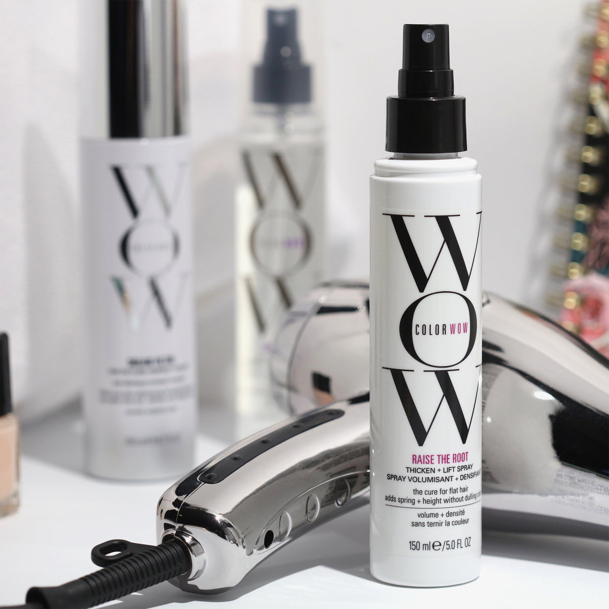 Eine Flasche Color Wow Raise The Root Thicken & Lift Spray ist mit einem Föhn und anderen Color Wow-Produkten auf einer weißen Oberfläche abgebildet.