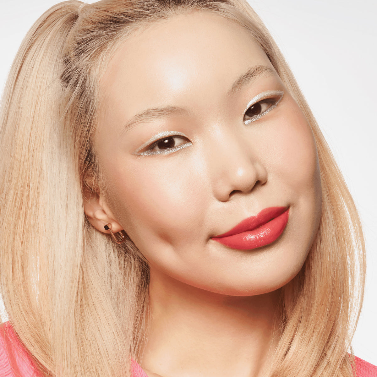 Person mit hellem Teint und blondierten Haaren lächelt und präsentiert den BABY GOT GLOW liquid highlighter 30 auf den Wangen.