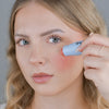Eine Frau trägt den Blush Stick – 2-in-1 Creme Rouge mit Pinsel Blossom auf ihre Wange auf und blickt in die Kamera.