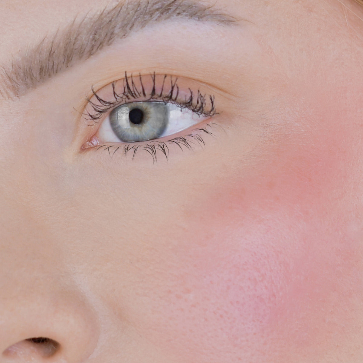 Nahaufnahme des Gesichts einer Person mit rosa Wangen geschminkt mit dem Blush Stick – 2-in-1 Creme Rouge mit Pinsel.