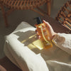 Eine Hand hält eine Flasche Pore Cleansing Oil PHA auf einem weißen Tuch, wobei das Sonnenlicht einen Schatten wirft.