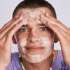 Eine lächelnde Person trägt Feel Pure Exfoliation Cleanser auf ihr Gesicht und schaut dabei in die Kamera.