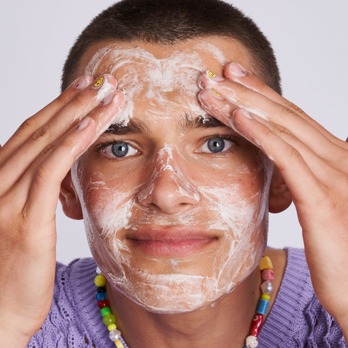 Eine lächelnde Person trägt Feel Pure Exfoliation Cleanser auf ihr Gesicht und schaut dabei in die Kamera.