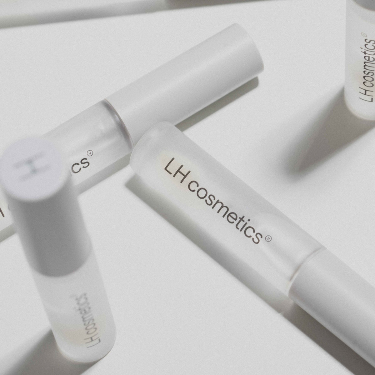 Drei mattierte Tuben Gloil von LH Cosmetics sind auf einer weißen Oberfläche mit weichen Schatten dargestellt.