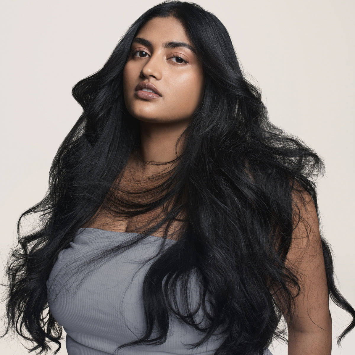 Frau mit langem, welligem, schwarzem Haar, gestylt mit dem Living Proof Perfect Hair Day 5-in-1-Styling Treatment.