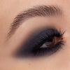 Nahaufnahme eines Auges mit dramatischem Smokey-Eye-Look in tiefem Anthrazit, weich verblendet bis über die Lidfalte hinaus. Die Wimpern sind lang und geschwungen.