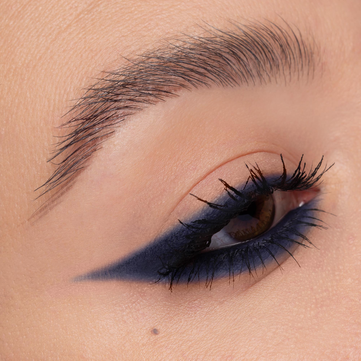 Nahaufnahme eines Auges mit kantigem, blauem Winged-Liner-Look. Der Liner verläuft spitz nach außen, die Wimpern sind definiert.