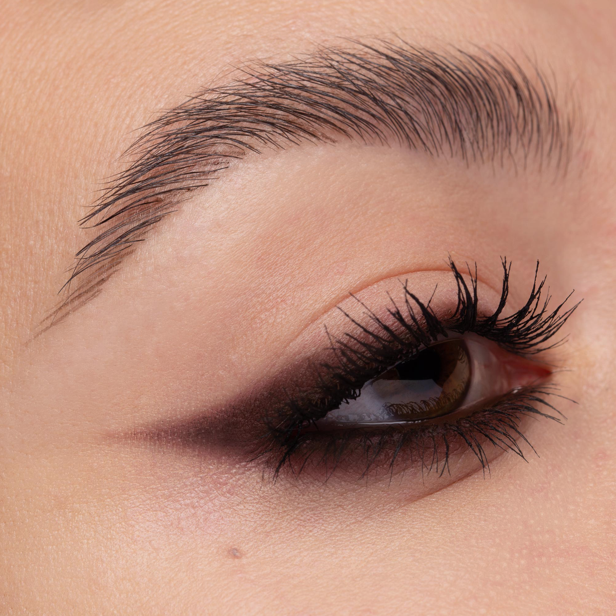 Nahaufnahme eines Auges mit kantigem, beerenfarbigem Winged-Liner-Look. Der Liner verläuft spitz nach außen, die Wimpern sind definiert.
