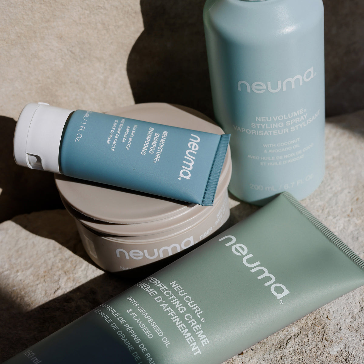 Neuma NEU CURL™ PERFECTING CRÈME und weitere Neuma produkte in zartem Grün und Beige, angeordnet auf einer Steinoberfläche.
