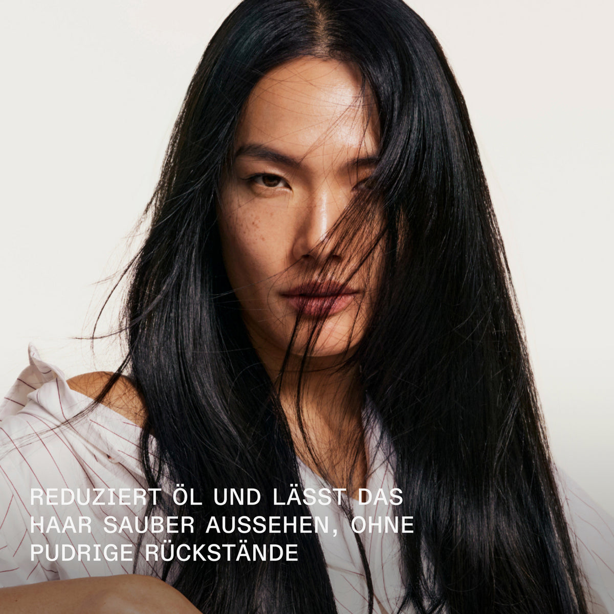 Eine Frau mit langem, schwarzem Haar blickt in die Kamera; der deutsche Text hebt hervor, wie das Trockenshampoo N° 4D Clean Volume Detox die Fettproduktion reduziert und für frisches, sauber aussehendes Haar sorgt.