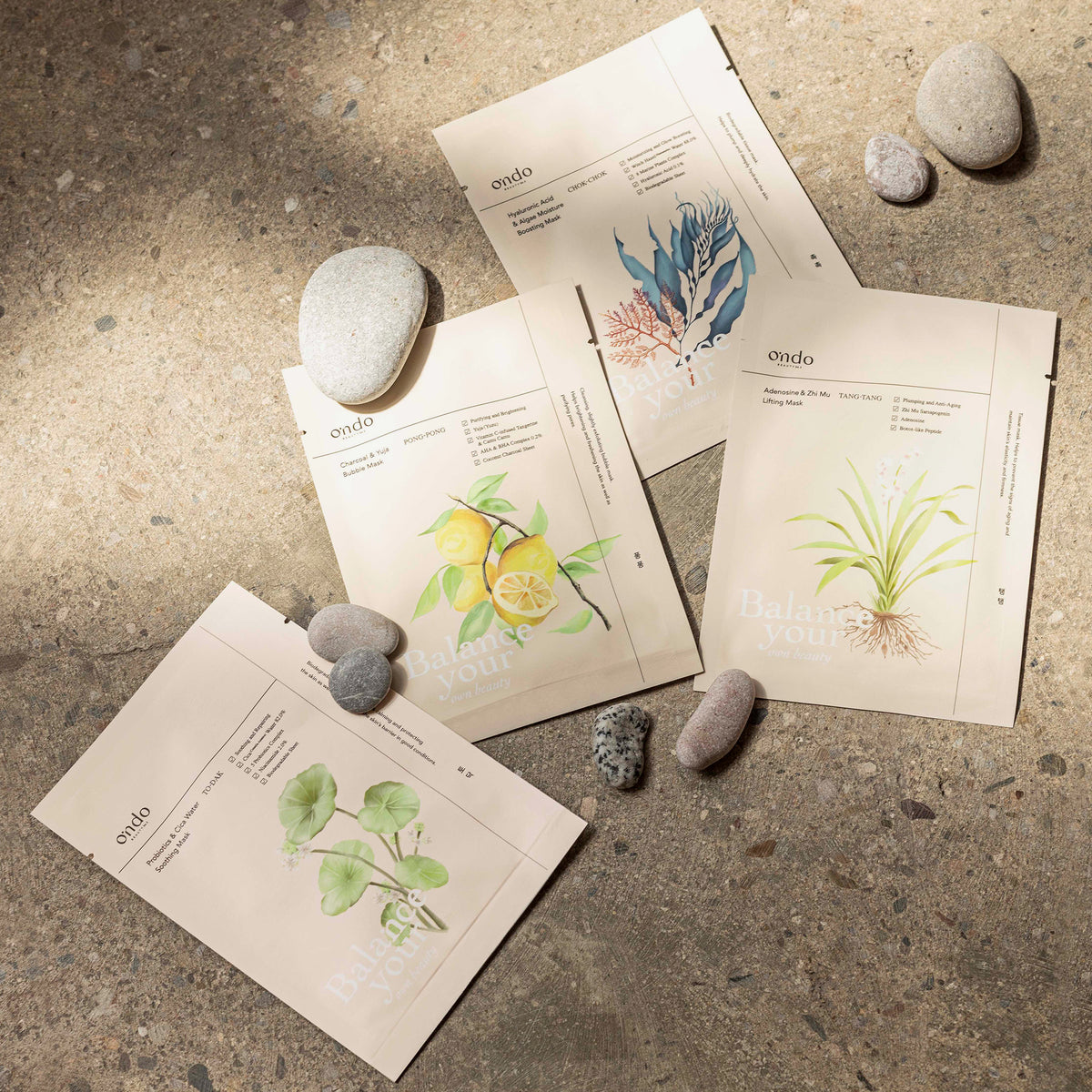 Vier Päckchen mit Augenmasken und glatten Steinen, angeordnet auf einer sonnenbeschienenen, strukturierten Oberfläche.