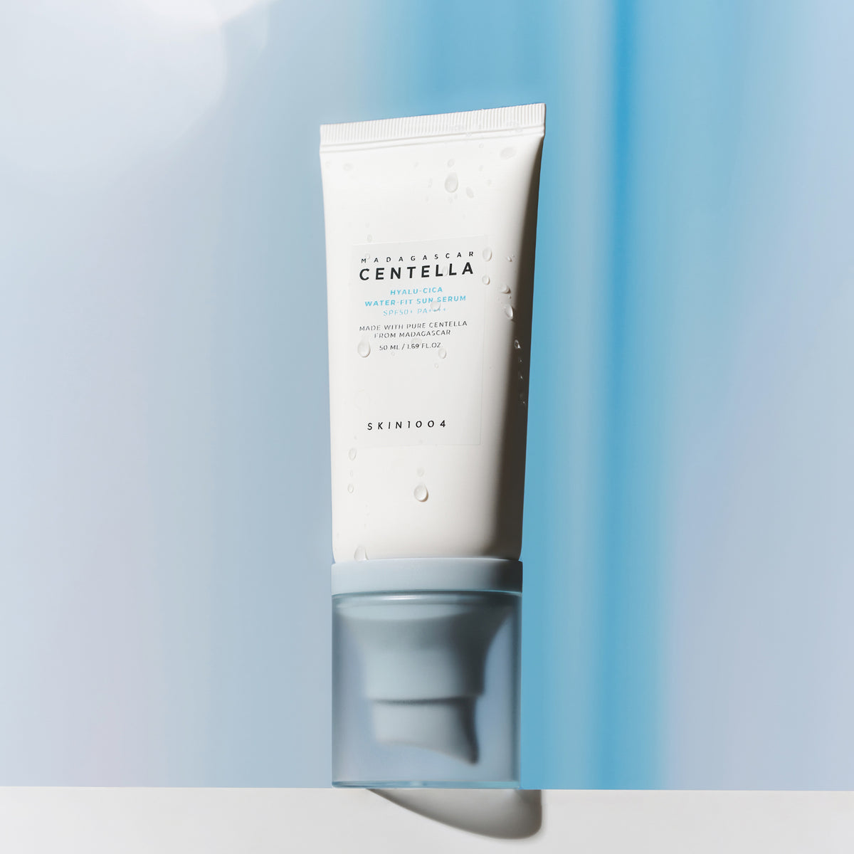 Eine weiße Tube Madagascar Centella Hyalu-Cica Water-Fit Sun Serum steht aufrecht vor einem blau-weißen Hintergrund.