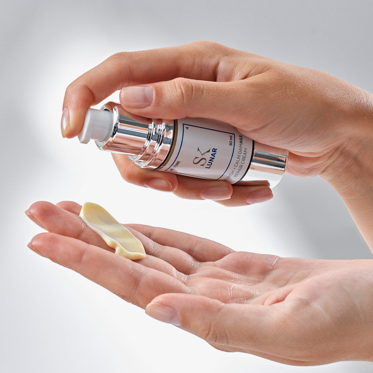 Zwei Hände dosieren eine beige Creme aus einer silber-weißen Flasche mit der Aufschrift „SK Lunar“ auf die Handfläche.