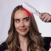Eine Frau lächelt, während sie die STYLPRO Re-Growth Red Light Hair Brush auf ihrer Kopfhaut anwendet. Die roten LED-Lichter leuchten dabei.