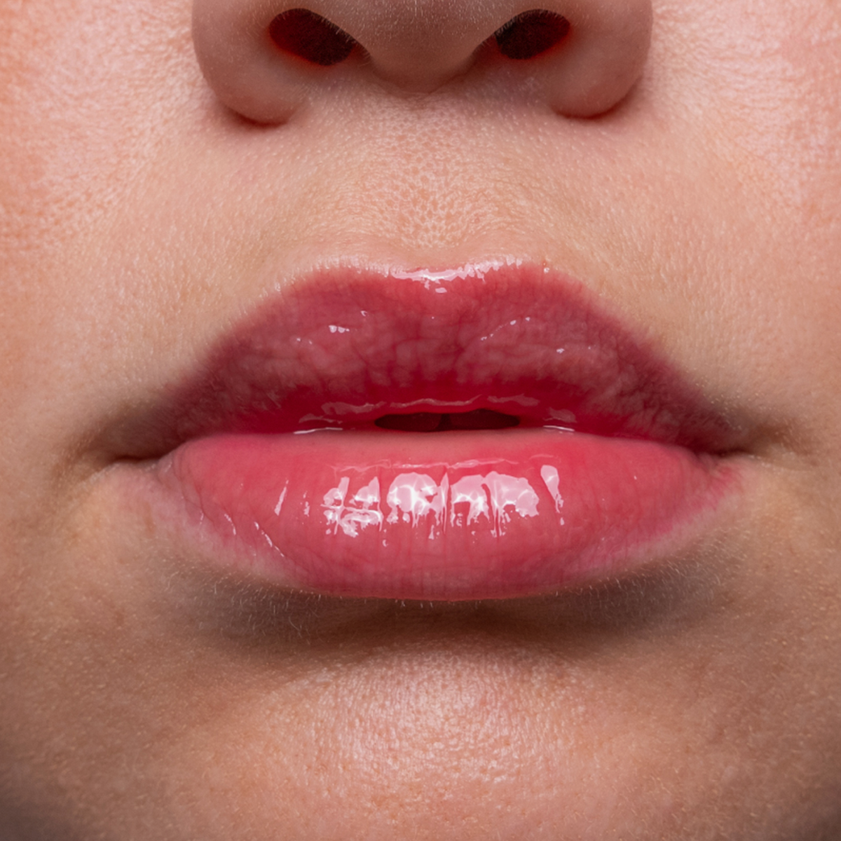 Nahaufnahme von glänzenden, rosa Lippen und einem Teil einer Nase auf glatter, heller Haut.