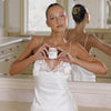 Eine Person in einem Seidenkleid hält im Badezimmer das Gradual Face Tan und schaut in die Kamera