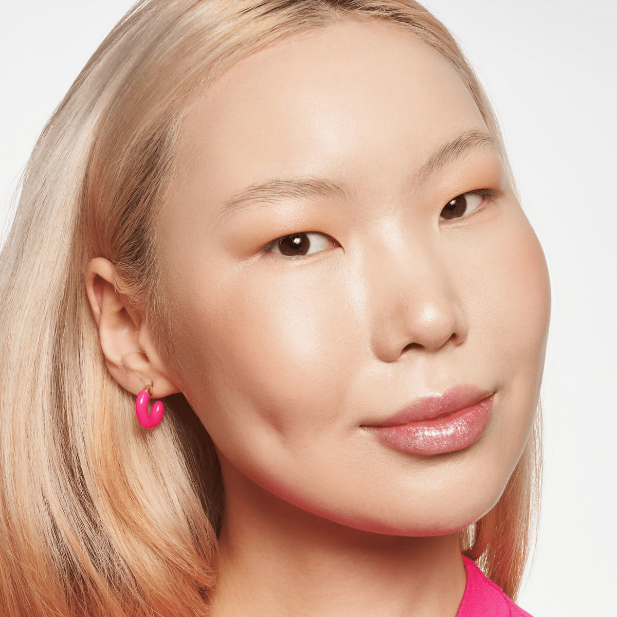 Person mit hellem Teint und blondierten Haaren lächelt und präsentiert den BABY GOT GLOW liquid highlighter 10 auf den Wangen.