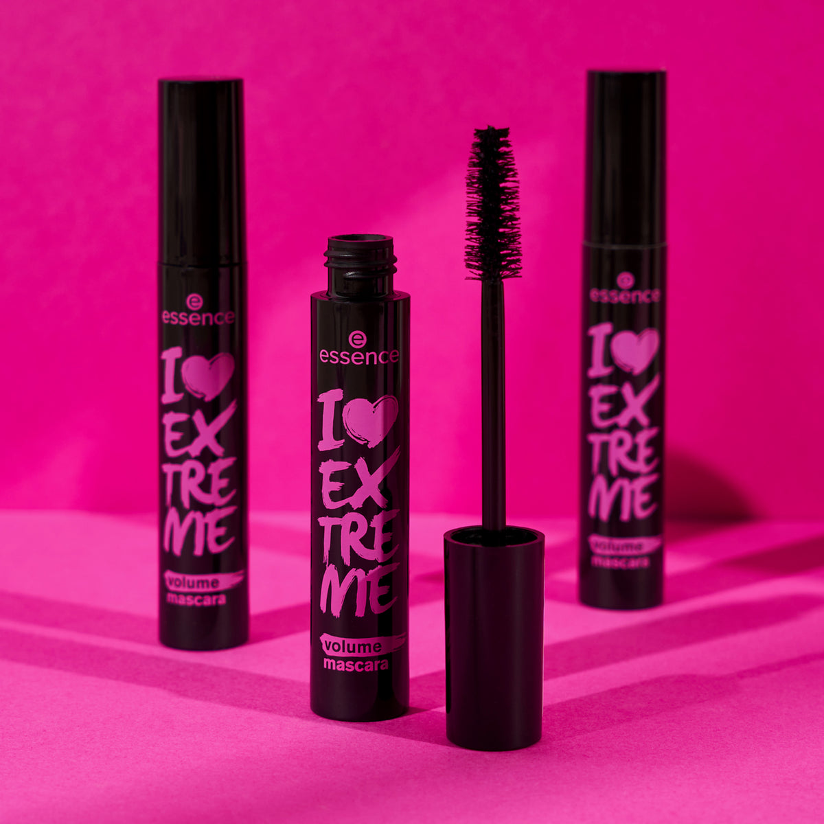 Drei Tuben I LOVE EXTREME Volume Mascara 01 auf rosa Hintergrund, wobei eine Tube geöffnet ist und die Bürste zu sehen ist.