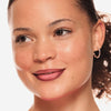 Eine lächelnde Person mit lockigem braunem Haar trägt Line n‘ STAIN! TATTOO LIP LINER vor einem weißen Hintergrund.
