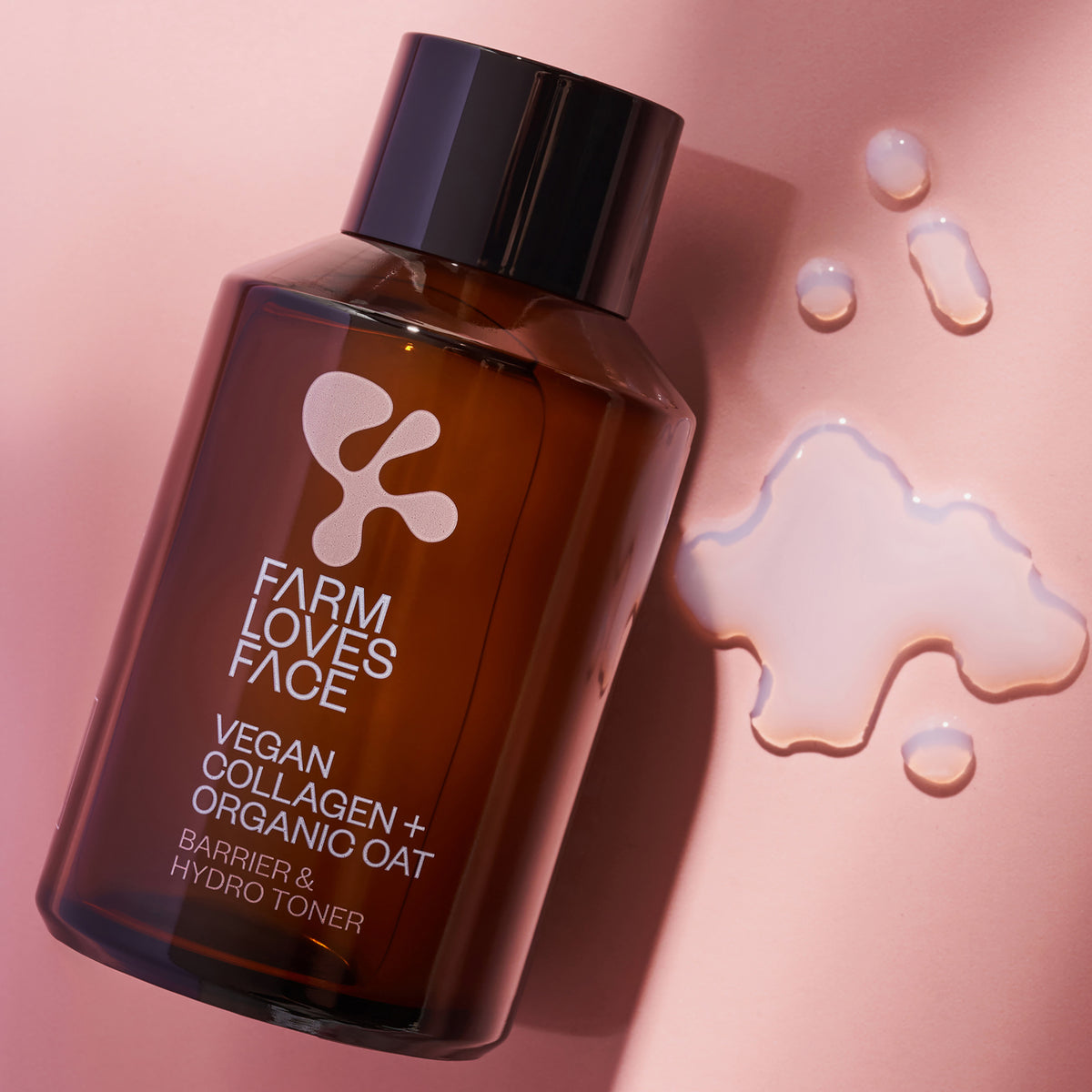 Braune Flasche Vegan Collagen + Organic Oat Barrier & Hydro Toner auf einer rosa Oberfläche mit verschüttetem Toner.