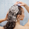 Eine Frau wäscht ihr lockiges Haar und verwendet die maria nila Stimulating Scalp Brush um das Shampoo einzumassieren.