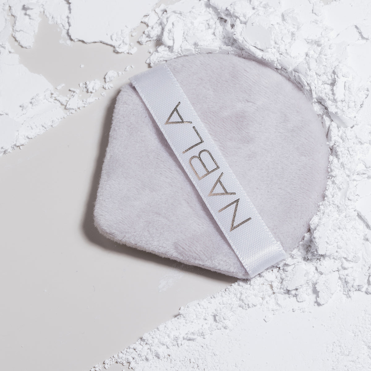 Ein weicher Make-up-Quast der Marke NABLA liegt auf einer Oberfläche, die mit Close-up Blotting Pressed Powder bestäubt ist.