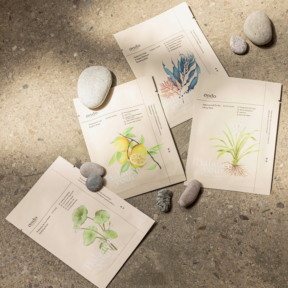 Vier Päckchen Gesichtsmasken von ondo und glatte Steine sind auf einer strukturierten Oberfläche im natürlichen Licht angeordnet.