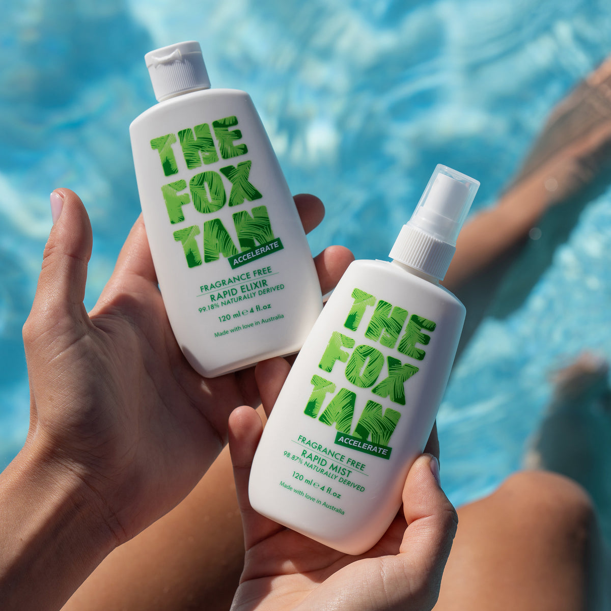 Zwei Hände halten zwei Flaschen Fox Tan aus der PURISH Summer Bag 2025 in der Nähe eines Pools, im Hintergrund sind Beine und Wasser zu sehen.