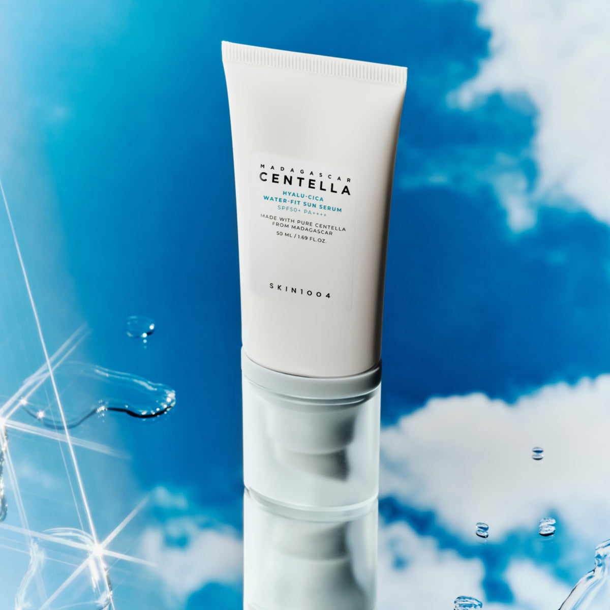 Eine Tube Madagascar Centella Hyalu-Cica Water-Fit Sun Serum steht aufrecht vor einem blauen Himmel mit Wolken und Wassertropfen.