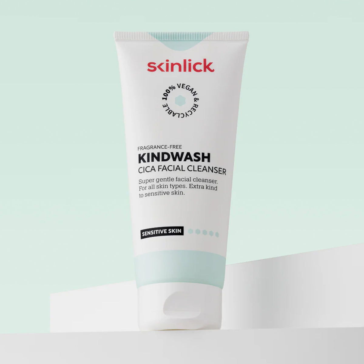 Weiße Tube des Skinlick Kindwash Cica Facial Cleansers mit rotem Logo, stehend vor mintgrünem Hintergrund auf weißer Fläche.
