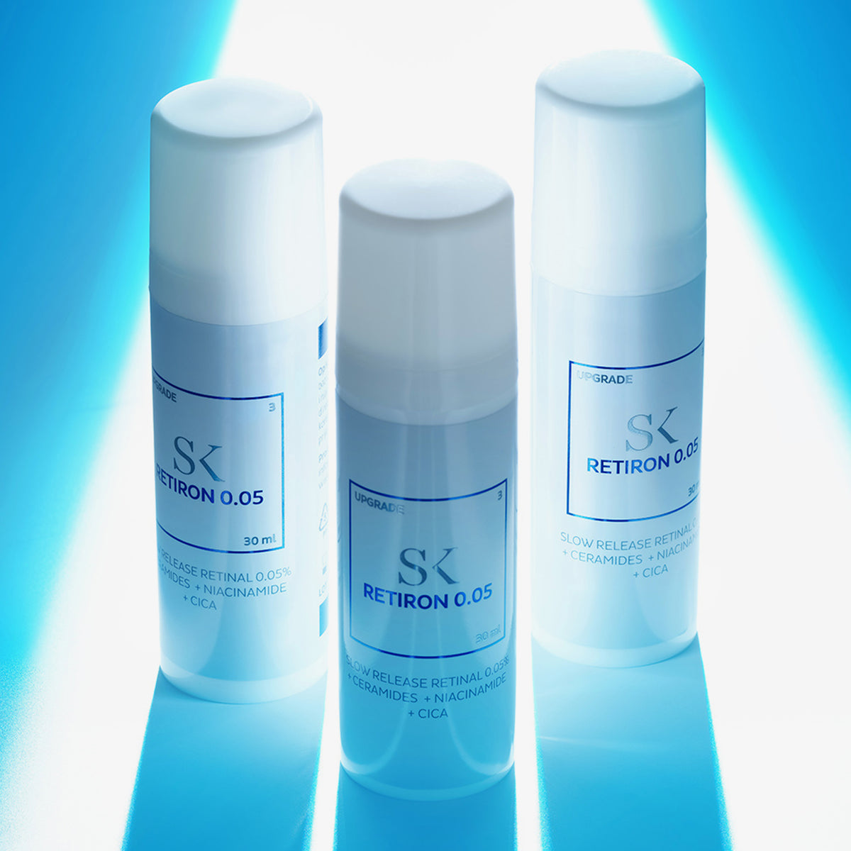 Drei Flaschen Retiron 0,05 Hautpflegeprodukt stehen vor einem leuchtend blauen Hintergrund und werden durch gezieltes Licht hervorgehoben.