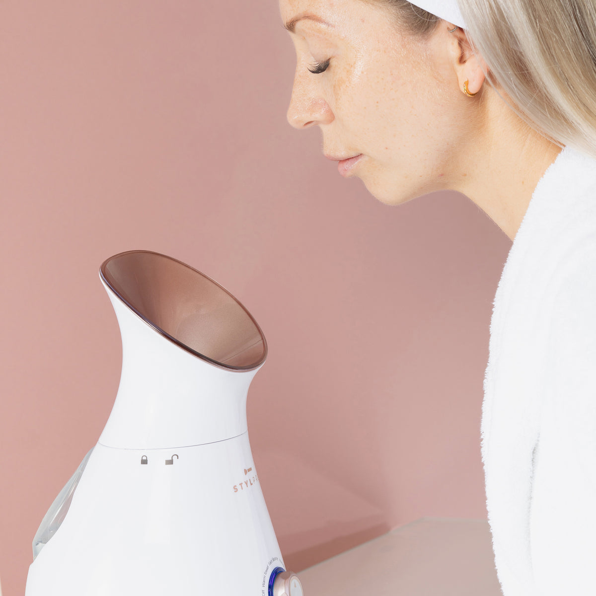 Eine Frau mit Stirnband verwendet den 4-in-1-Gesichtsdampfer vor einem rosa Hintergrund.