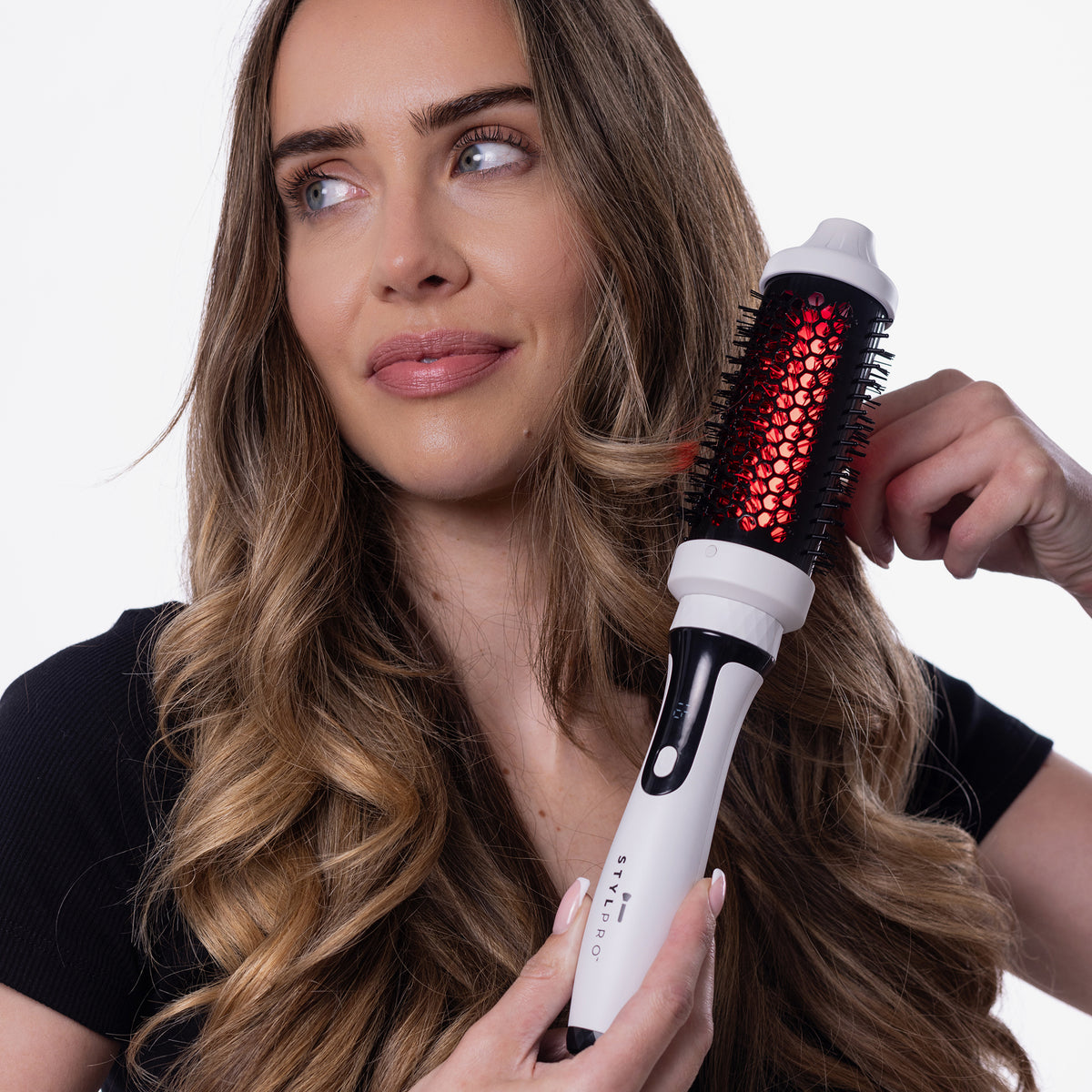 Eine Frau lockt ihr langes Haar mit der rot leuchtenden STYLPRO Near-Infrared Heated Hairbrush vor einem weißen Hintergrund.