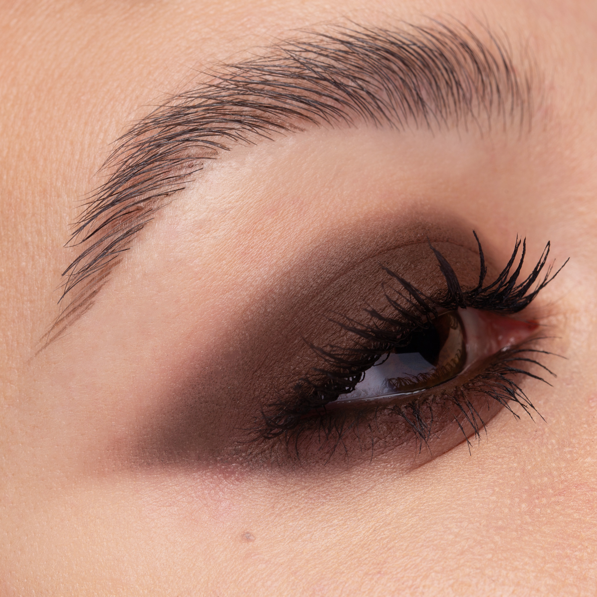 Nahaufnahme eines Auges mit dramatischem braunem Smokey-Lidschatten und langen, definierten Wimpern.
