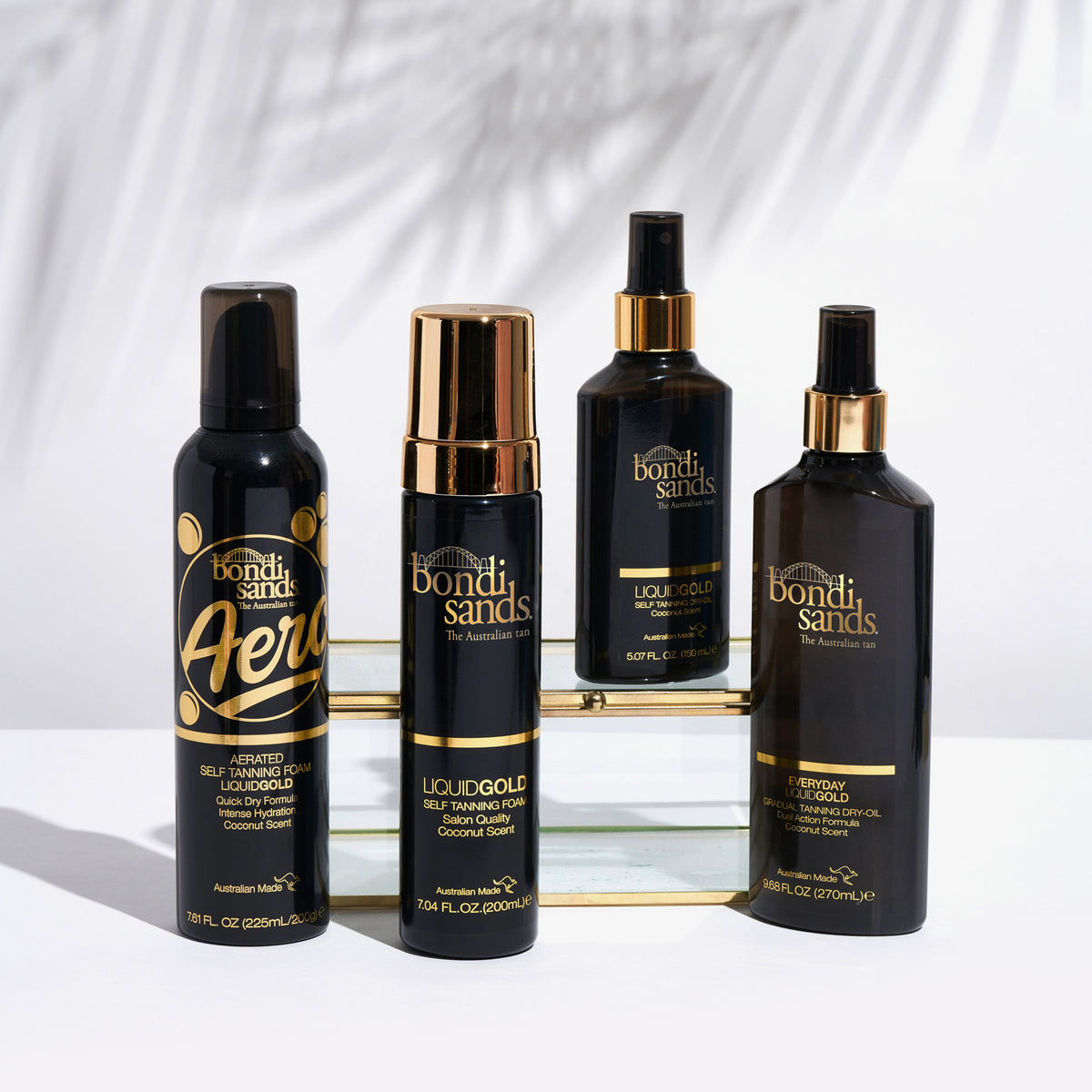 Vier Bondi Sands Liquid Gold Bräunungsprodukte in dunklen Flaschen auf weißer Oberfläche