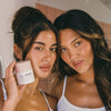 Zwei Frauen mit langen dunklen Haaren lächeln sanft, während sie mit dem Gradual Face Tan von Bali Body posieren
