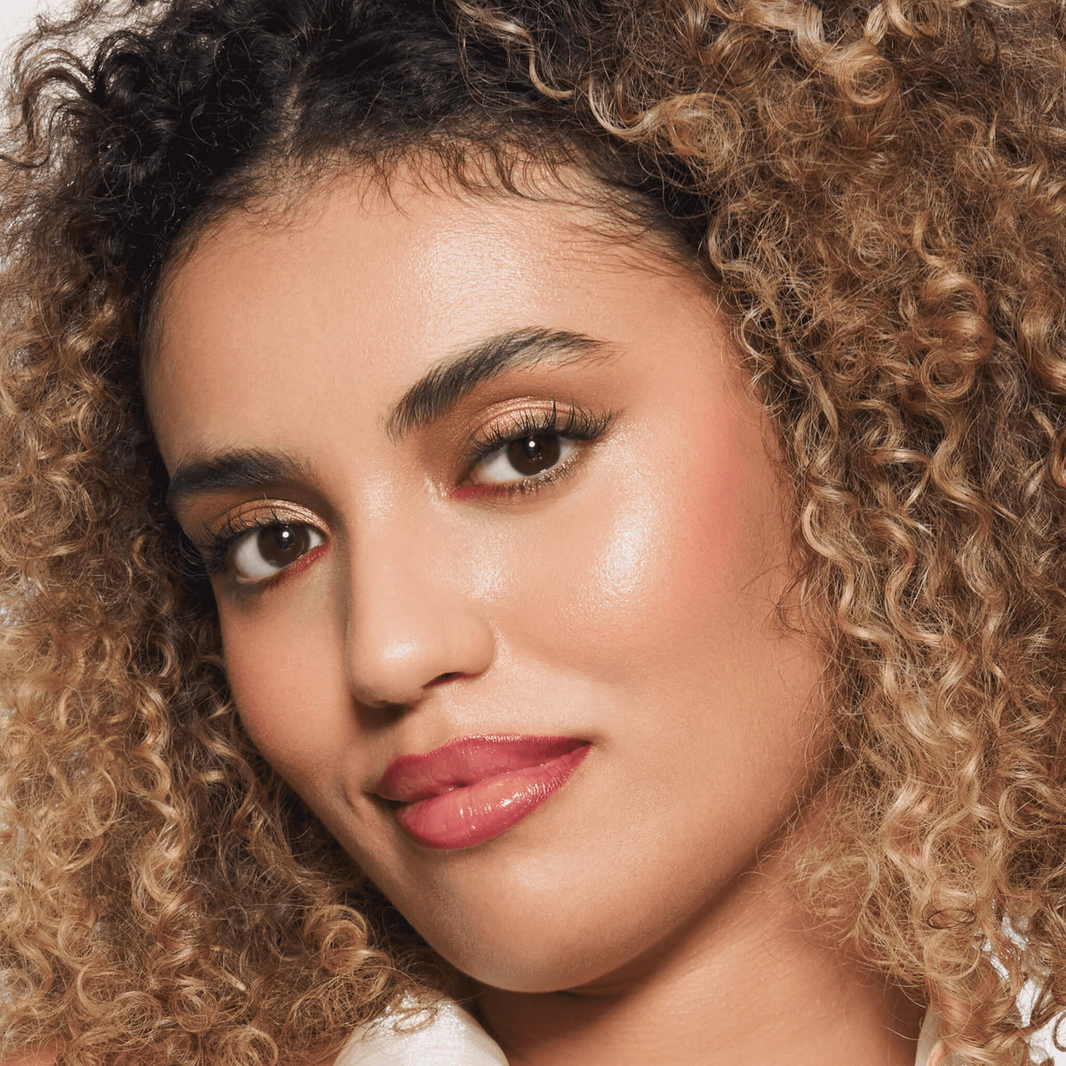 Eine Frau mit lockigem blondem Haar und strahlendem Make-up, hervorgehoben durch den Slim'Matic Ultra Precise Brow Pencil Waterproof 040, lächelt in die Kamera.