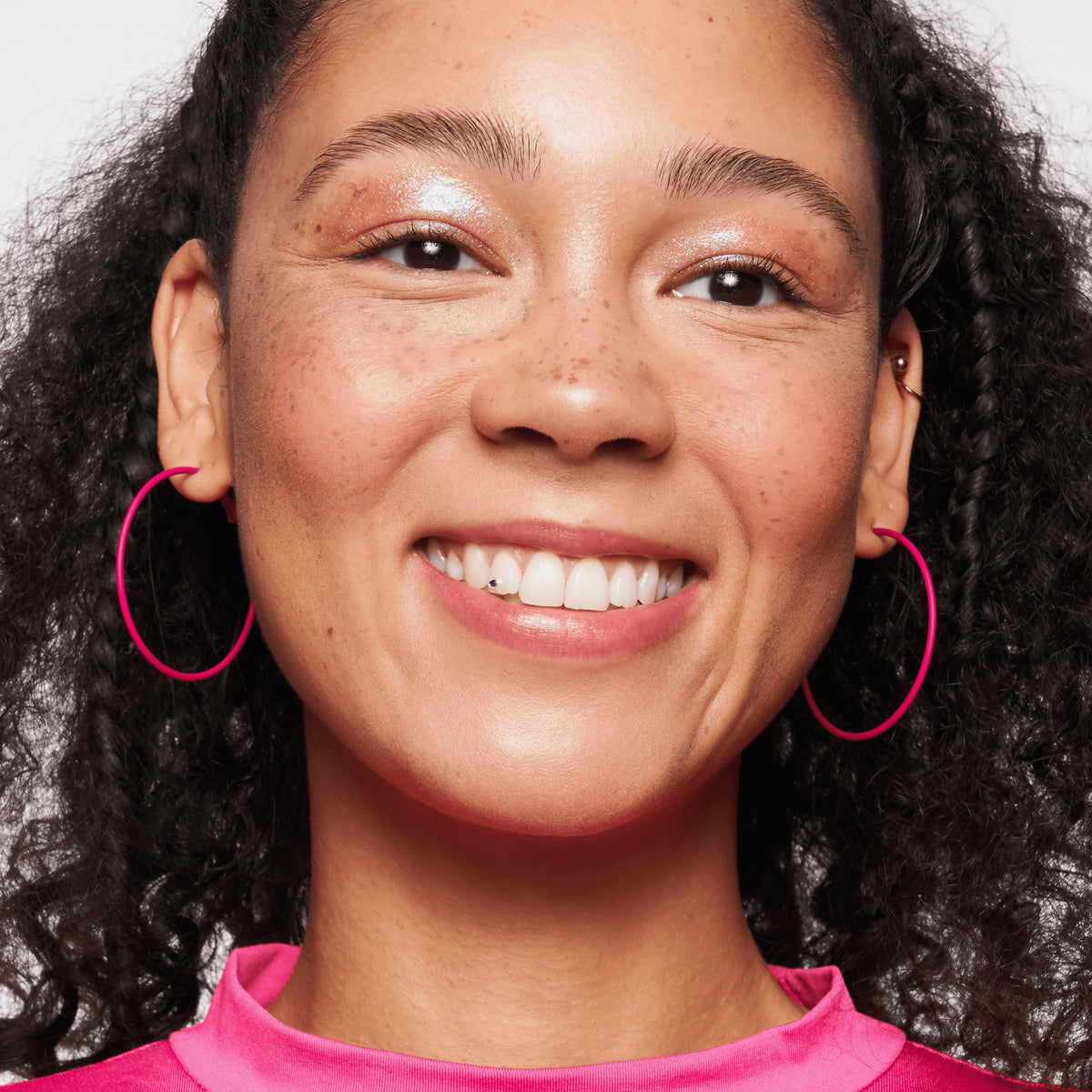 Person mit mittlerem Teint und dunklen Haaren lächelt und präsentiert den BABY GOT GLOW liquid highlighter 30 auf den Wangen.