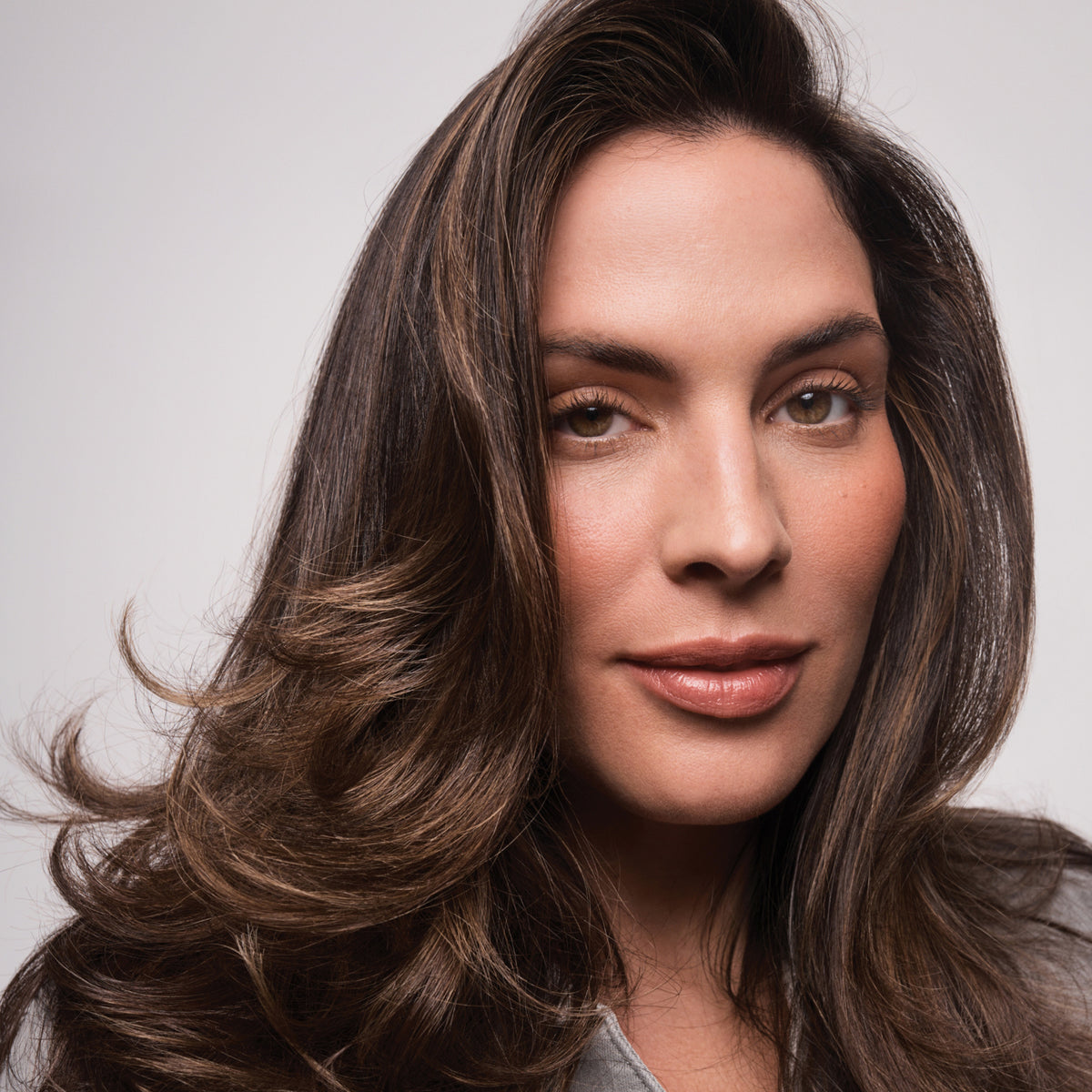 Eine Frau mit langem, welligem braunem Haar präsentiert den voluminösen Effekt des Living Proof Full Volume & Root-Lifting Spray.