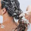 Person, die ihr langes, dunkles Haar mit Living Proof Perfect Hair Day Shampoo wäscht.