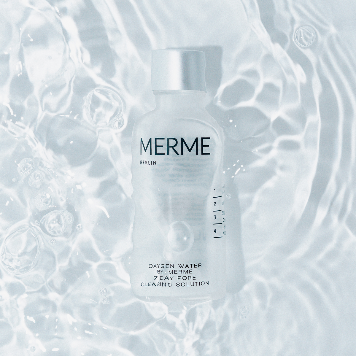 Eine Glasflasche MERME Oxygen Water mit silbernem Deckel schwimmt in klarem Wasser, das durch Lichtreflexe beleuchtet wird.