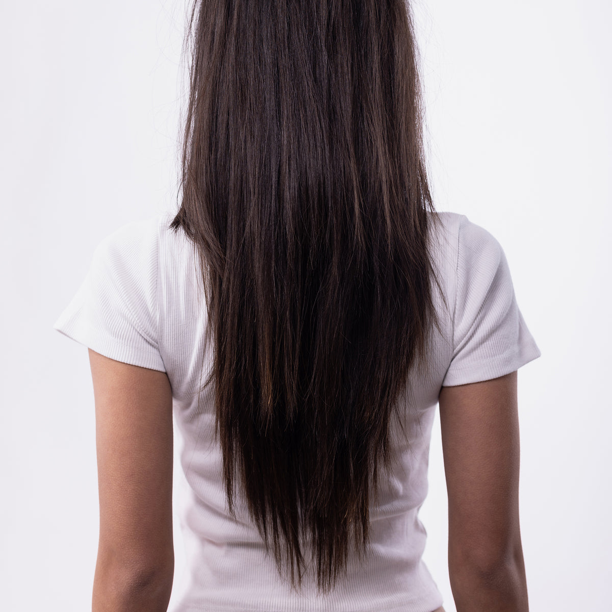 Rückansicht einer Frau mit langem, glattem, dunklem Haar in weißem Shirt – Ergebnis vor dem Styling mit der StylPro Wärmebürste.