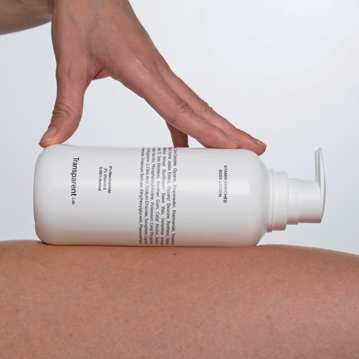 Hand hält eine weiße Flasche der Transparent Lab Vitamin Enriched Body Lotion über einem Bein; Produkt wird zur Anwendung vorbereitet.