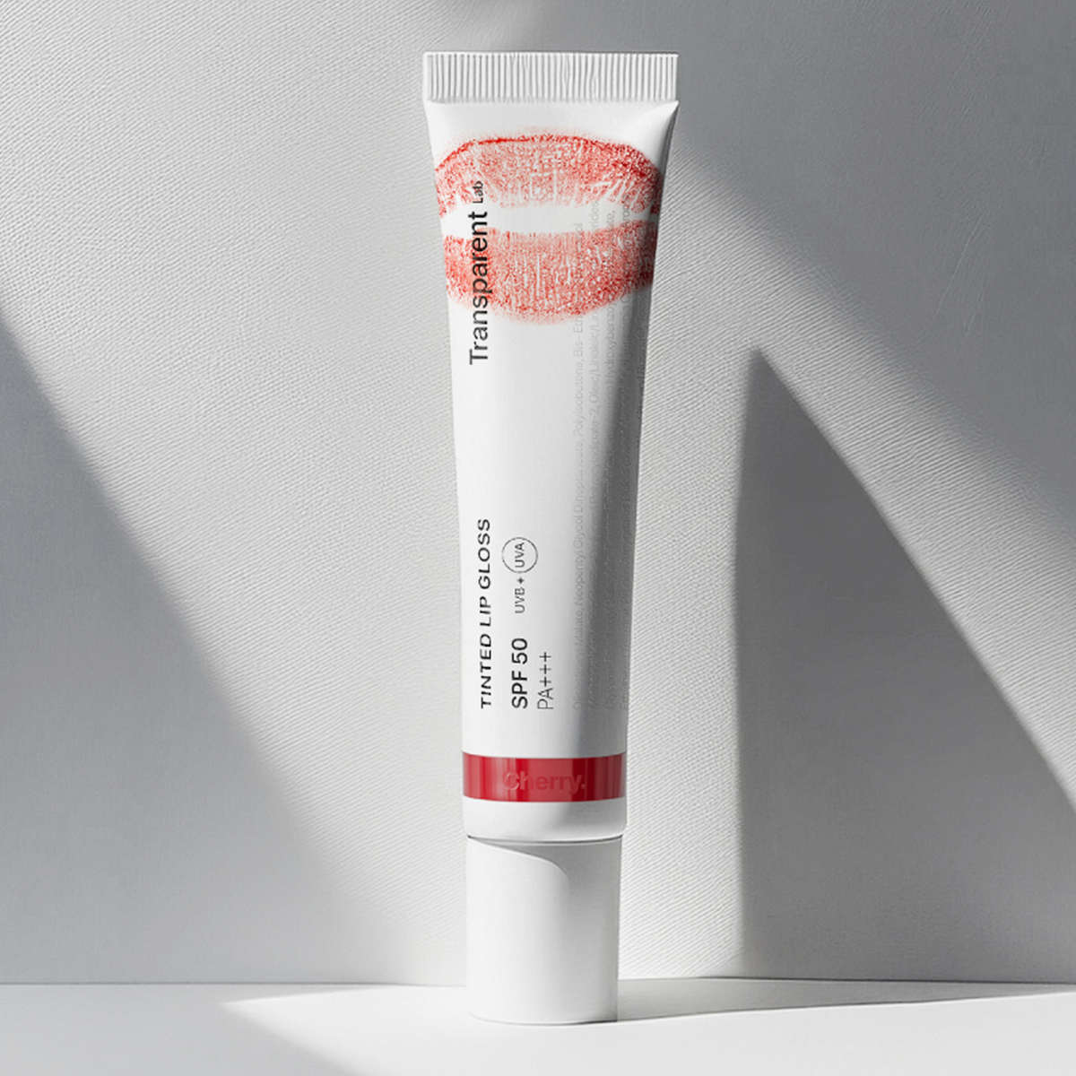 Auf einer weißen Fläche steht eine Tube getönter Lipgloss SPF50 mit einem roten Lippenstift-Kussabdruck auf der Tube.