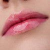 Nahaufnahme der Lippen einer Person mit heller Haut mit dem Glossin‘ Glow Tinted Lip Oil 010 in glänzendem rosa Farbton.
