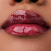 Nahaufnahme der Lippen einer Person mit brauner Haut mit dem Glossin‘ Glow Tinted Lip Oil 010 in glänzendem rosa Farbton.